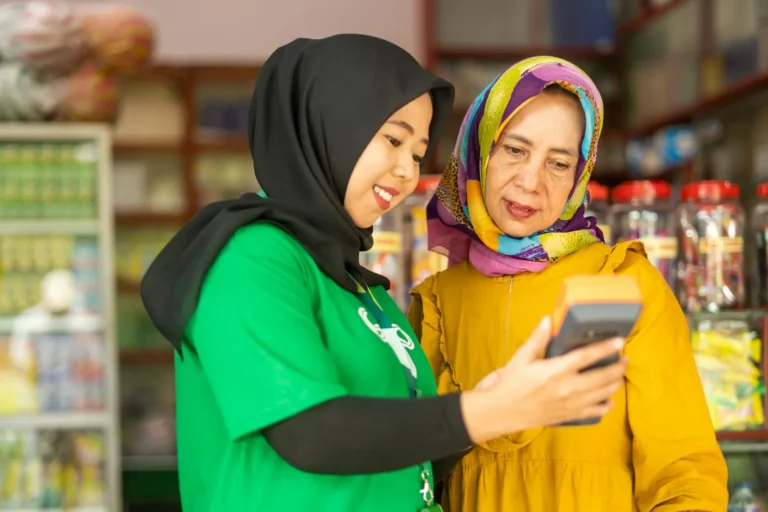 A shop assistant showing a customer a message on her phone, the kind a WhatsApp broadcast message reaches
