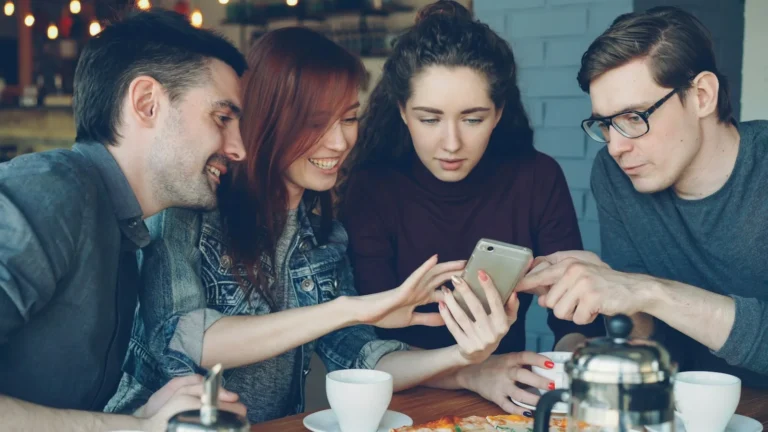 Four people gathered around a single phone screen at a table