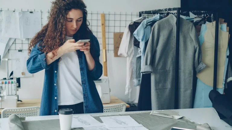 A boutique owner messaging customers on her phone beside a clothing rail