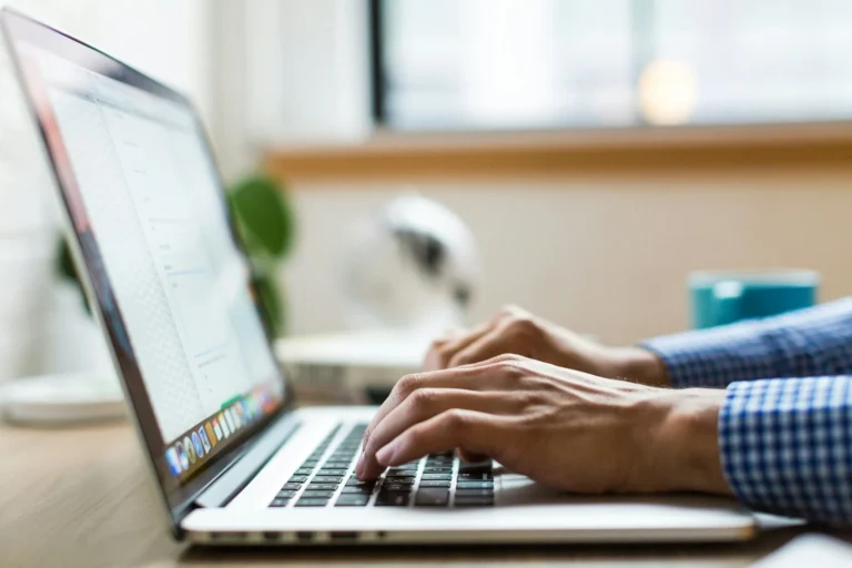 Hands typing a document on a laptop at a desk by a window, the daily work of content marketing services