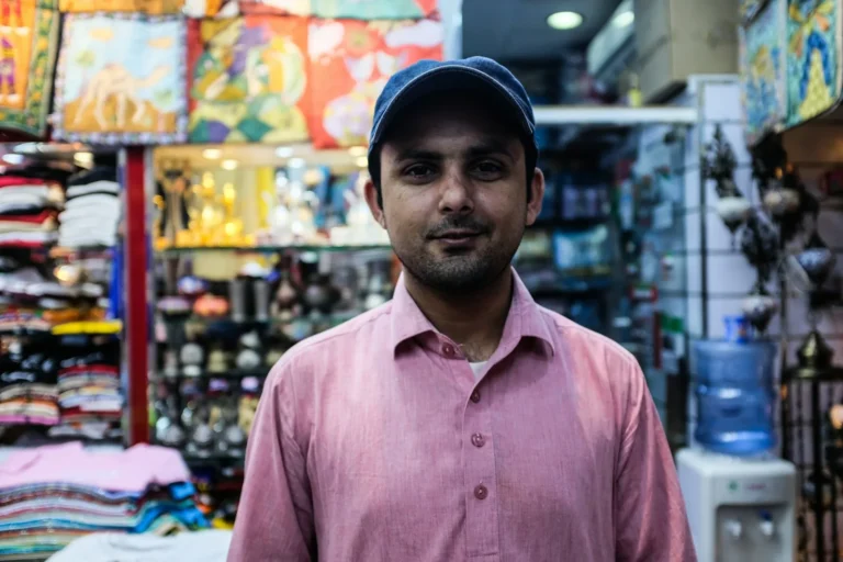 Shop owner in a pink shirt and cap standing inside his store
