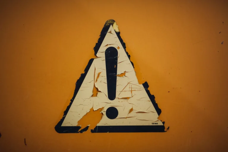 Worn exclamation-mark warning sign painted on an orange wall