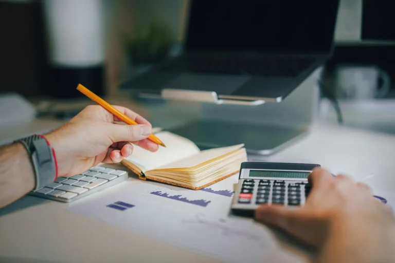 Person using a calculator and taking notes in a notebook at a desk