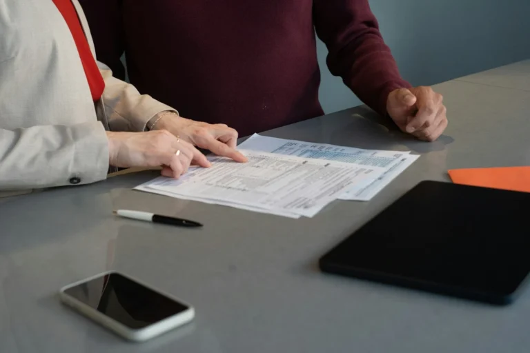Two people comparing printed documents side by side on a table
