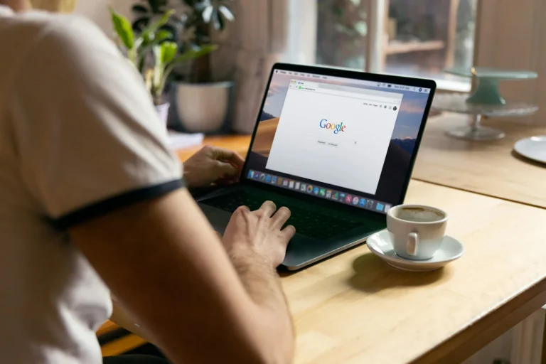 Person typing a search into Google on a laptop beside a cup of coffee