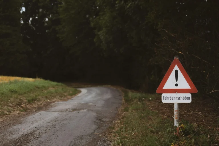 Red triangle warning sign standing beside a narrow country road