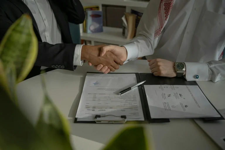Two businessmen shaking hands over a signed contract on a desk