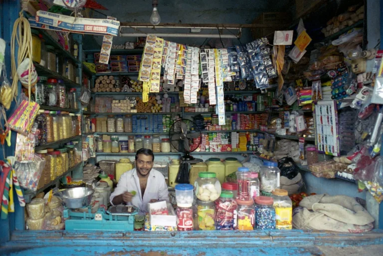 Smiling shopkeeper behind the counter of a packed neighbourhood general store