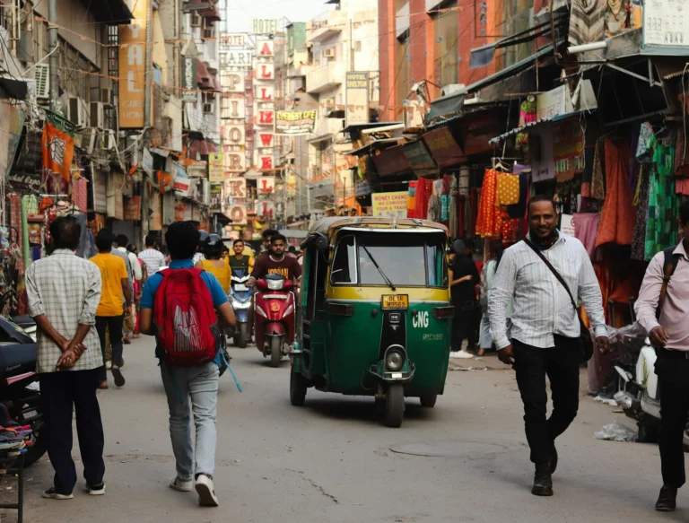 Busy Delhi market street with an auto rickshaw and shoppers between shopfronts
