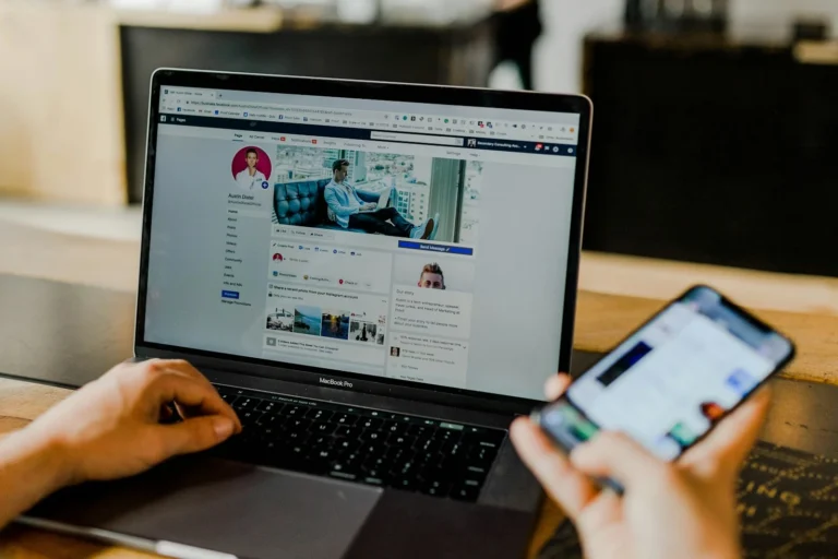 Person scrolling a social media feed on a phone while a business profile is open on a laptop