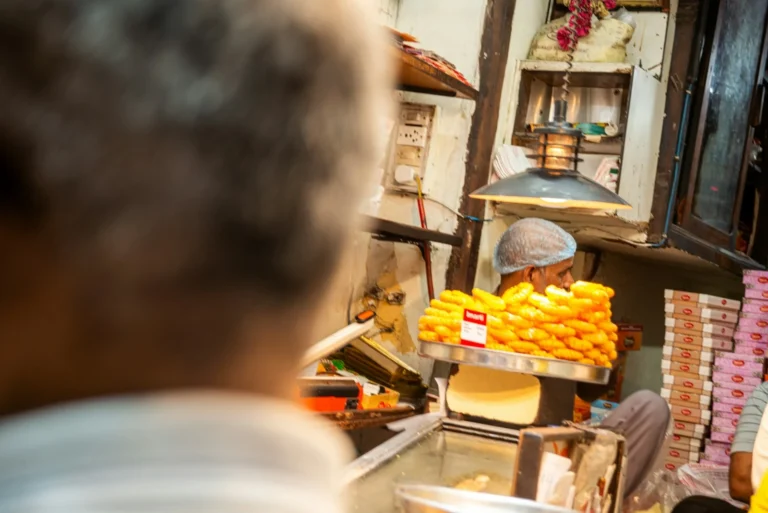 Vendor at a sweet shop counter piled with fresh jalebi and mithai