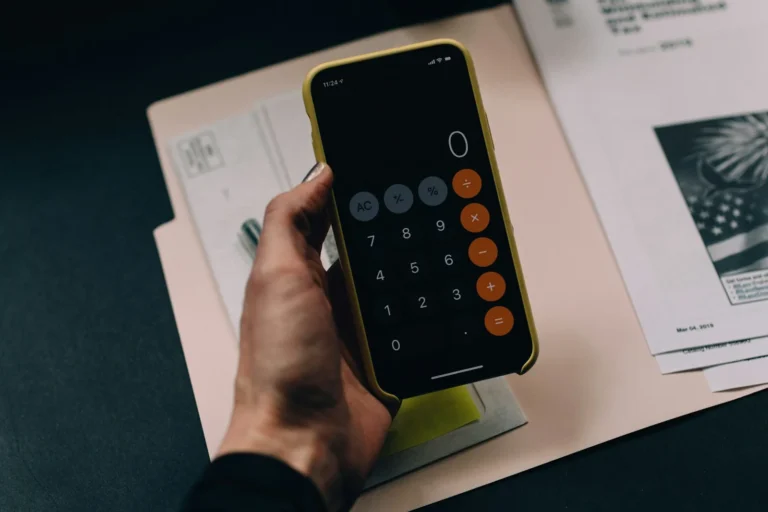 Hand holding a smartphone calculator above a folder of paperwork