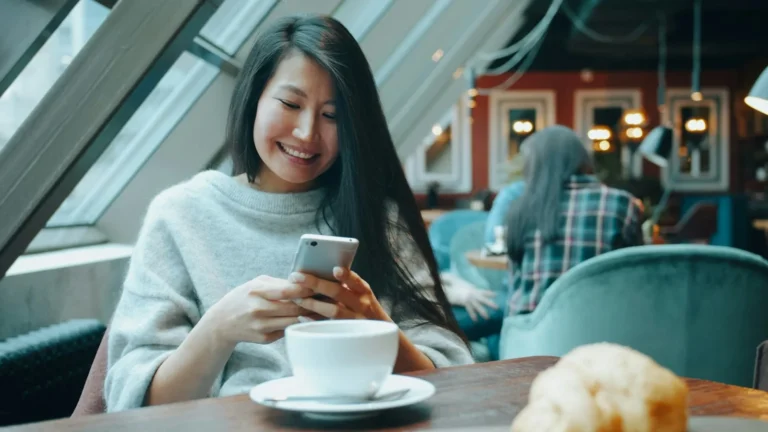 Woman smiling at her phone in a cafe, scrolling through WhatsApp Status ads
