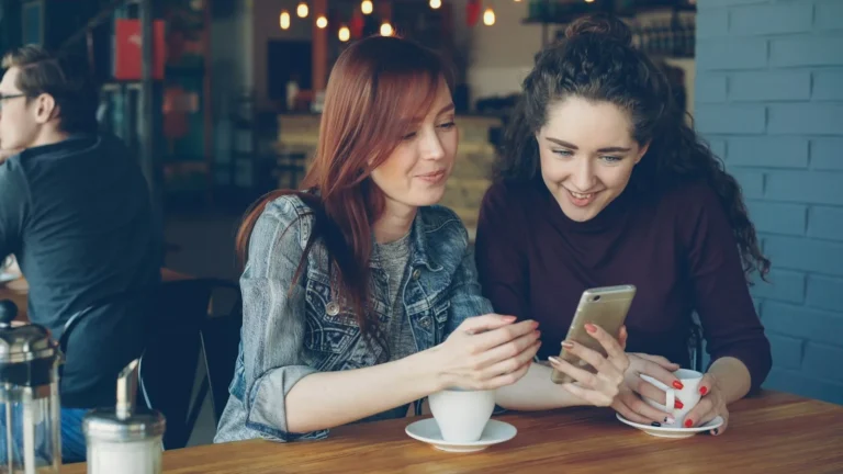 Two friends looking at a phone together, the Status feed where WhatsApp Status ads appear