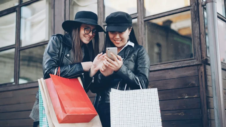 Two women with shopping bags looking at a phone, a local audience for Status ads