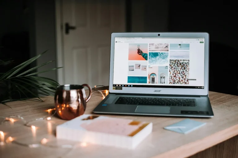 A laptop on a desk showing a website with a copper mug and a notebook beside it